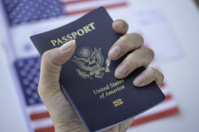 Female fingers holding Passport of USA on blurred American flag background.